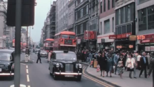 1960年代のロンドン ストリートは典型的な1960年代の服を着た人々でいっぱいです アイコニックな黒いタクシーと赤いダブルデッカーバスが道路を移動します リアルタイムカラーアーカイブビデオ — ストック動画