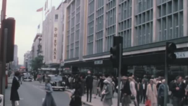 1960年代のロンドンのショッピング地区のオックスフォード ストリートの道路を横断する人々 背景にある黒いタクシーの駐車場 典型的な1960年のファッション バスに身を包んでいる — ストック動画