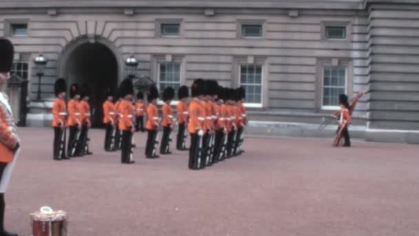 1970年代のこのヴィンテージアーカイブは ロンドンのバッキンガム宮殿で画期的な軍事的伝統を示し コールドストリームガードが旗で行進しています — ストック動画