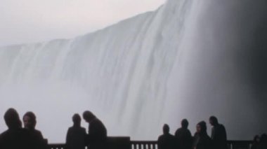 Siyah turist siluetleri Niagara Şelaleleri 'nden akan suyun muazzam hacmine hayret ediyor. 1970 'lerin bu benzersiz arşiv görüntüleri bu ikonik doğanın harikasını ve ölçeğini yakalıyor.