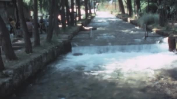 自然公園内の人工的な流れの中で水を流れる 観光客はテーブルに座って食べる 休暇中の穏やかな人々のリラックスしたシーン JajceのPlivsko Jezero湖 1970年ボスニアのアーカイブ映像 — ストック動画