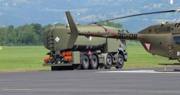 2023年6月4日 スロベニア 燃料タンカートラックが軍用飛行場で給油するためのカモフラージュグリーンの軽量軍用ヘリコプターに近づき 明確な空と遠い山々 — ストック動画