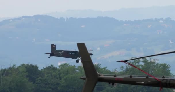 2023年6月4日 スロベニア 小型プロペラの軍用輸送機が着陸に近づき 低高度で飛行し 駐車したヘリコプターの背後で速度を上げる スロベニア空軍のピラトスPc 6ポーター — ストック動画