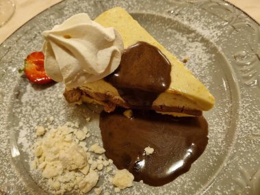 Bol çikolata soslu, taze çilek ve çırpılmış kremayla süslenmiş lezzetli bir dilim peynirli kek.