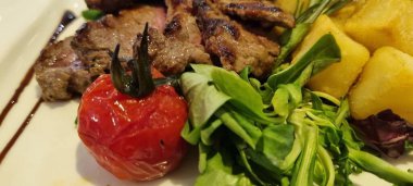 Kızarmış domates, patates ve taze salata ile sulu ızgara biftek.