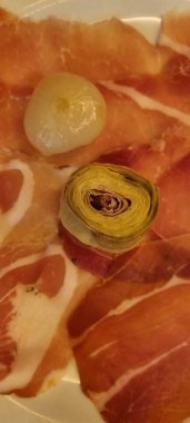 Close-up view of a platter featuring thinly sliced cured meats and marinated artichoke clipart