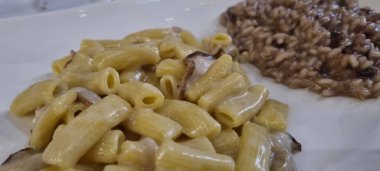 Lezzetli kremalı mantarlı makarnanın yakın plan çekimi yanında baharatlı risotto servis edilir.