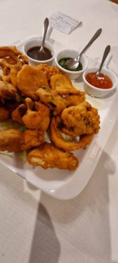 Beyaz bir tabakta çeşitli baharatlarla servis edilen lezzetli pakora böreklerinin üst görüntüsü.