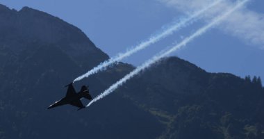 Mollis İsviçre 19 Ağustos 2023: Belçika Hava Kuvvetleri F-16 savaş uçağı, gelişmiş havacılık becerileri sergileyen hava gösterisi sırasında dağ zemininde duman izleriyle aerobatik manevra yaptı. 