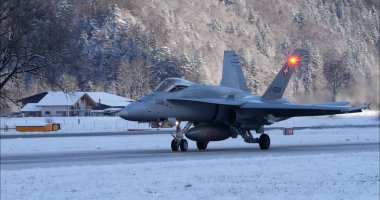 Meiringen İsviçre 19 Ocak 2023: Karlı bir pistte askeri jet taksisi ve kış operasyonları sırasında seyrüsefer ışıkları aydınlatıldı. Isı bozulması görülebilir. Uzayı kopyala İsviçre Hava Kuvvetleri F-18