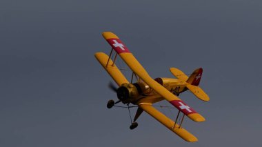 ECTOBER 06, 2024: Montagnana, İtalya: Sarı, klasik Bucker Bu 133 Jungmeister RC çift kanatlı bir uçağın bankacılık dönüşünde çekilmiş bir fotoğrafı, geniş bir kopya alanı olan gri gökyüzüne karşı izole edilmiş..