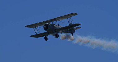 Hoher Kasten, İsviçre: Bir klasik çift kanatlı uçak, Boeing Stearman Modeli 75, açık mavi gökyüzü boyunca beyaz bir duman iziyle uçuyor..