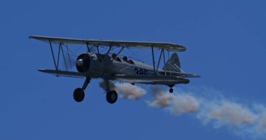 Hoher Kasten, İsviçre: Bir akrobatik çift kanatlı uçak, bir Boeing Stearman Modeli 75, açık mavi gökyüzüne doğru beyaz bir duman iziyle uçuyor. İsviçre bayrağı kuyrukta görünür.