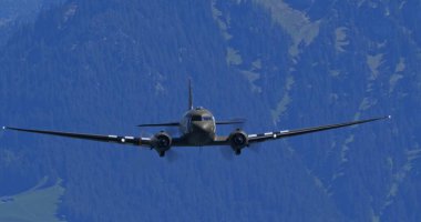30 Mayıs 2025 Hoher Kasten İsviçre: Douglas DC-3 C-47 Skytrain askeri nakliye uçağı, D-Day istila çizgilerine sahip, İsviçre Alpleri üzerinde alçak irtifada doğrudan kameraya doğru uçar..