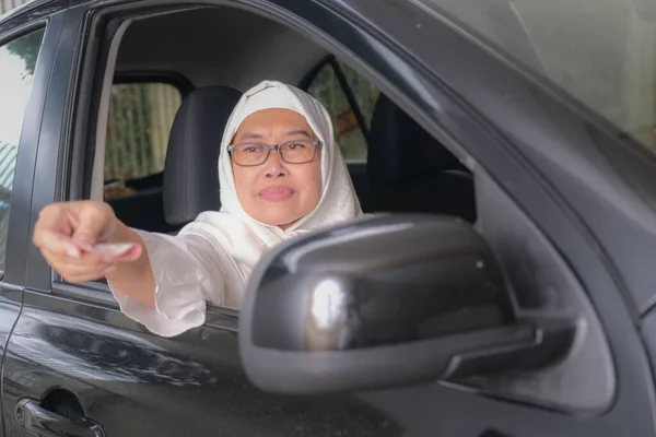 インドネシアの女性からお金を与えます彼女の車のステアリングホイールの後ろから — ストック写真