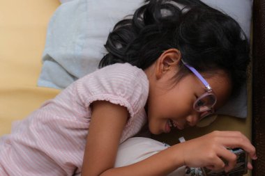 Kanepede uzanmış akıllı telefondan oyun oynayan küçük kız.