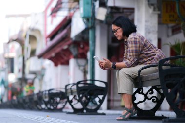 Malioboro caddesindeki bankta oturan Asyalı kadın akıllı telefonunu okuyor.