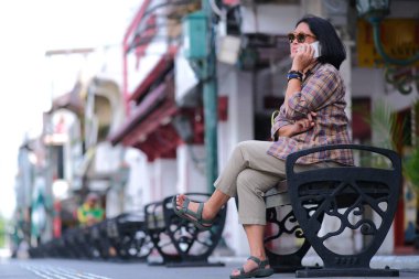 Yogyakarta 'nın ikonik Malioboro caddesinde bir bankta oturan Asyalı kadın bir telefon görüşmesi yapıyor.