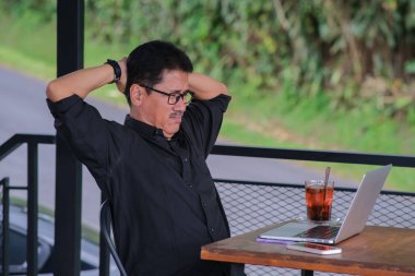 Oturan ve önünde diz üstü bilgisayarıyla çalışmaktan bıkmış görünen bir adam.