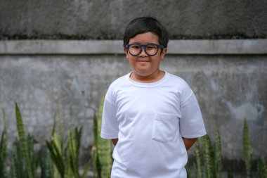 Tek başına duran Asyalı bir çocuk ve çok fazla video oyunu oynadığı için gözlük takıyor.