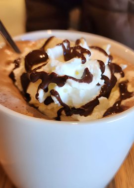 Krem şantili bir fincan kahve ve ahşap bir masada çikolata.