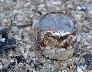 Paslı demirli metal fıçı kumun üzerinde yatıyor.