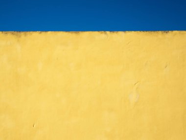 Arka planda mavi gökyüzü olan sarı beton bir duvar.