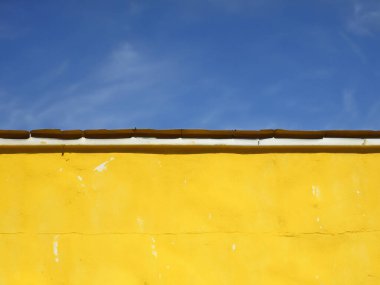Arka planda mavi gökyüzü olan sarı beton bir duvar.