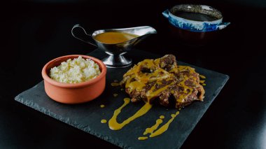 Veal osso buco with sauce presented on a slate plate accompanied by white rice and a metal sauce dish. Foodie. close-up. selective focus.