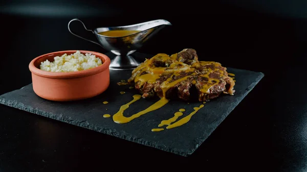 Veal osso buco with sauce presented on a slate plate accompanied by white rice and a metal sauce dish. Foodie. close-up. selective focus.
