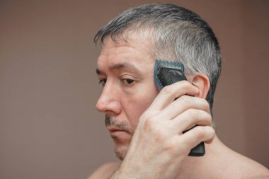 Man cutting his own hair with a clipper.
