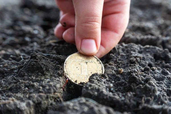 stock image The child's hand raises the Ukrainian one hryvnia coin lying in the black soil.