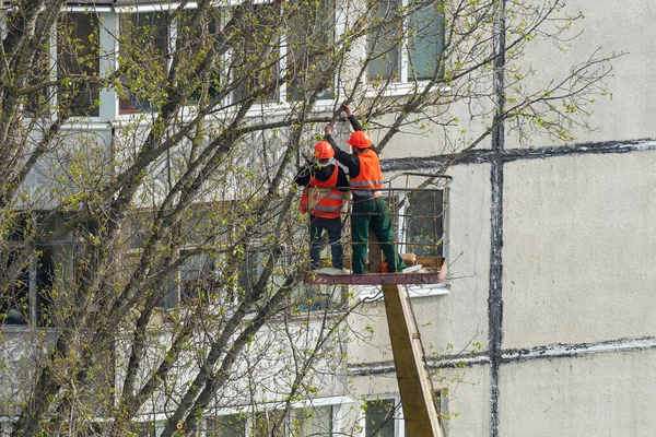 Workers in the city cut trees with a chainsaw while standing on a crane lift.