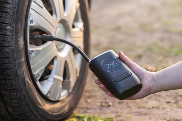 stock image A woman's hand holds a wireless portable air pump for inflating car tires.