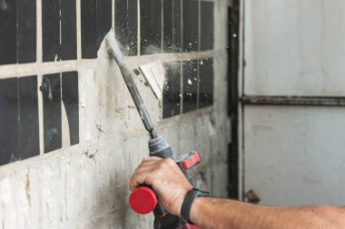 Builder with a puncher dismantles old tiles from a concrete wall.
