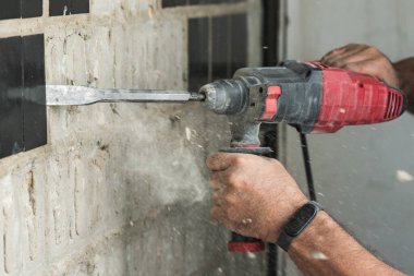 Builder with a puncher dismantles old tiles from a concrete wall.