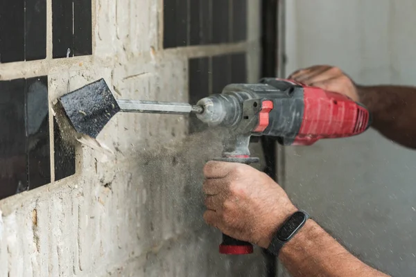 stock image Builder with a puncher dismantles old tiles from a concrete wall.