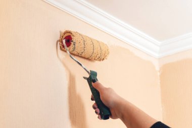 Bir kadının eli, bej rengi bir boya rulosuyla duvarı boyar..