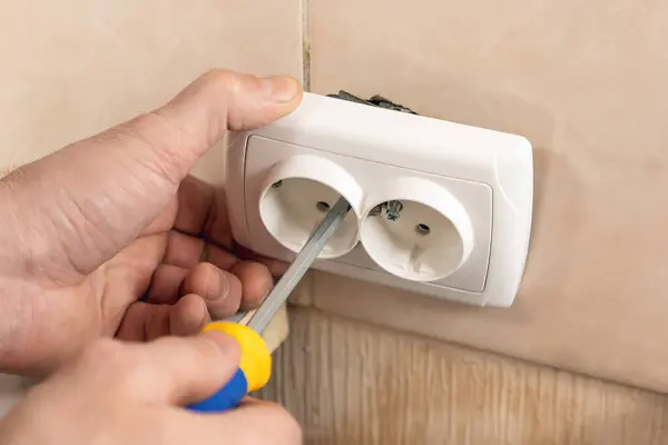 A man repairs an electrical outlet with a screwdriver.