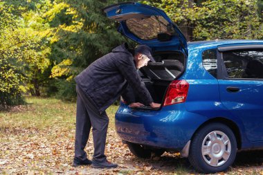 Bir adam sonbahar ormanında bir arabanın bagajına bakar..
