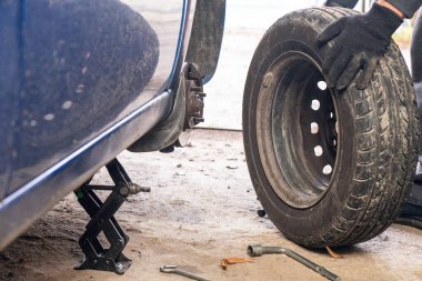 Adamın biri garajda tekerleği söküyor. Araba tekerlekleri değiştiriliyor.