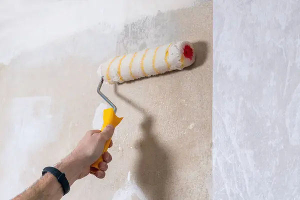A man uses a roller to apply glue to a wall to paste wallpaper. Room renovation.