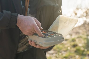 Balıkçının elleri çeşitli yem ve olta iğneleriyle dolu plastik bir kutu tutuyor..