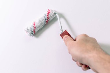 Bir adamın eli bir duvarı boya rulosuyla beyaza boyar..