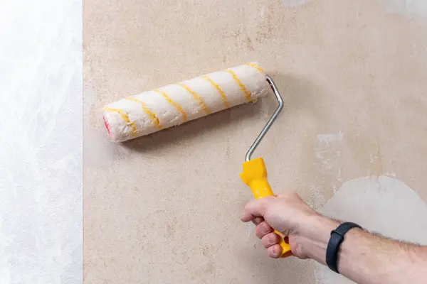 A man uses a roller to apply glue to a wall to paste wallpaper. Room renovation.