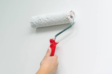 Bir kadının eli bir duvarı boya rulosuyla beyaza boyar..