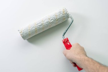 Bir adamın eli bir duvarı boya rulosuyla beyaza boyar..