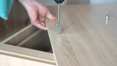 Tüy matkabıyla matkap kullanan bir işçi ahşap bir levhada delik açar.