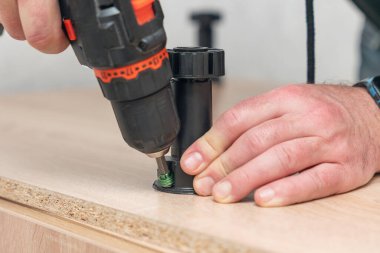 Mobilya monte eden bir adam, tornavidayla plastik bir bacak vidalıyor..