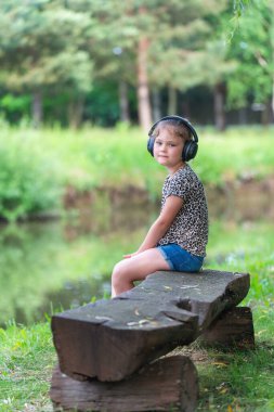 Modern kablosuz kulaklıklı şirin küçük kız açık havada müzik dinlemeyi seviyor..